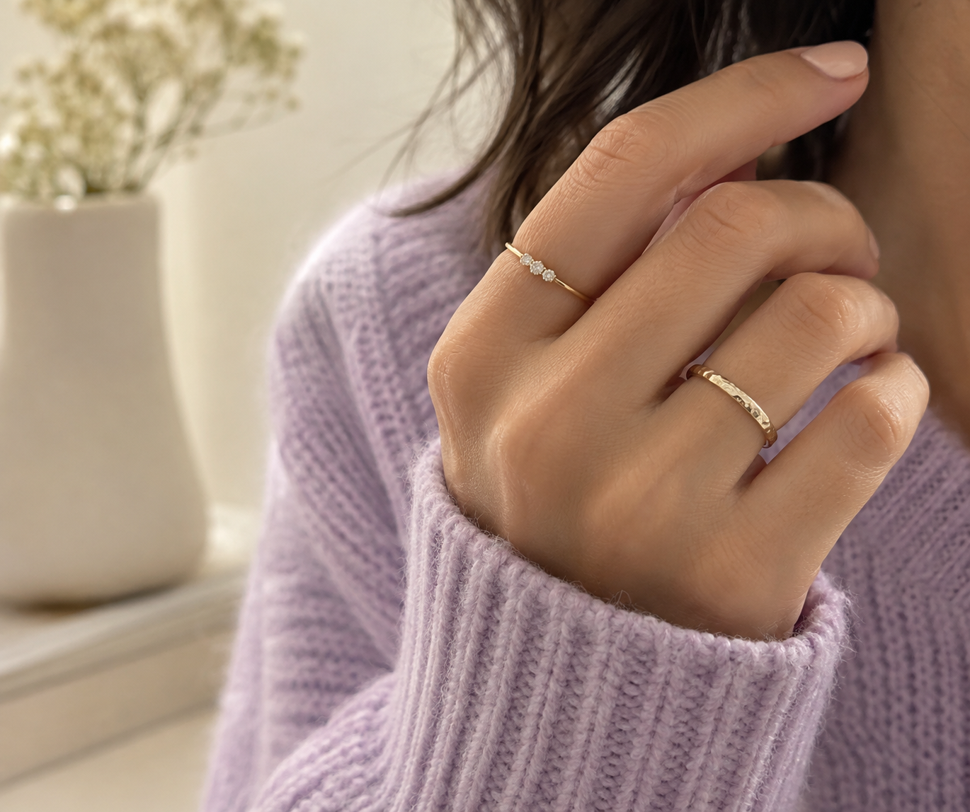 Mano con dos anillos delicados combinados de forma cómoda junto a un sweater lila