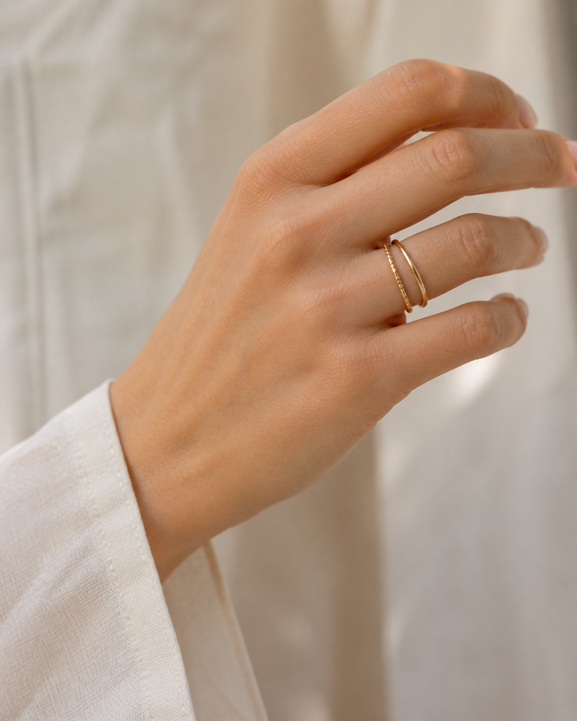 Mano con dos anillos dorados delicados y camisa de lino clara