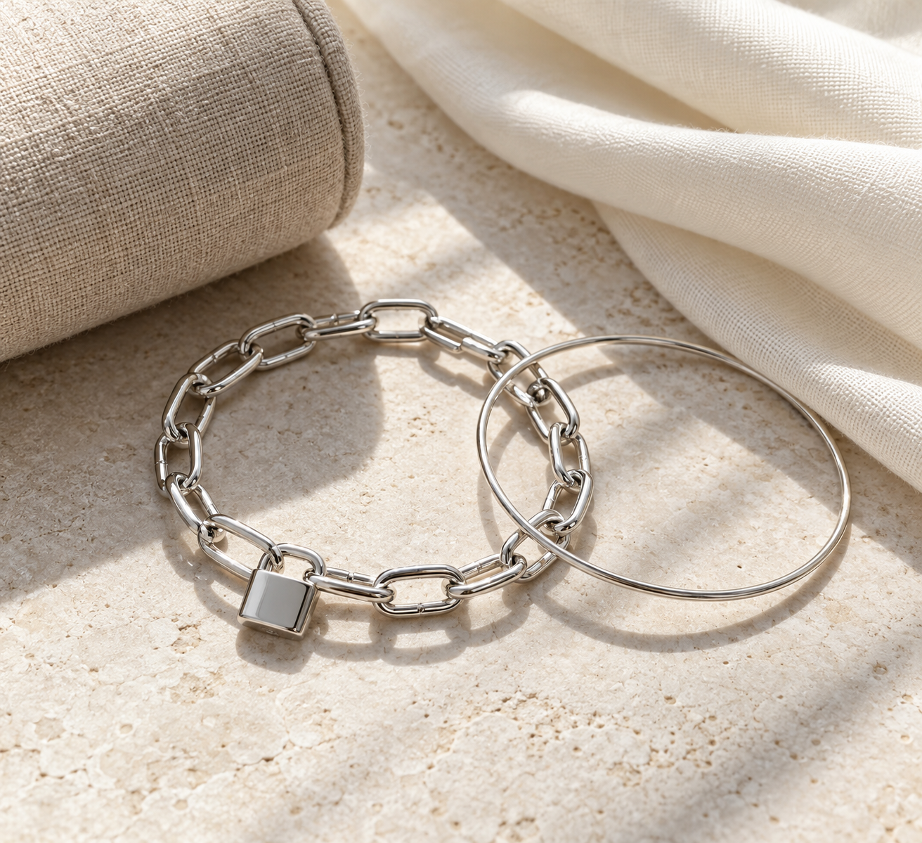 Pulsera candado plateada combinada con una pulsera fina de aro sobre lino claro