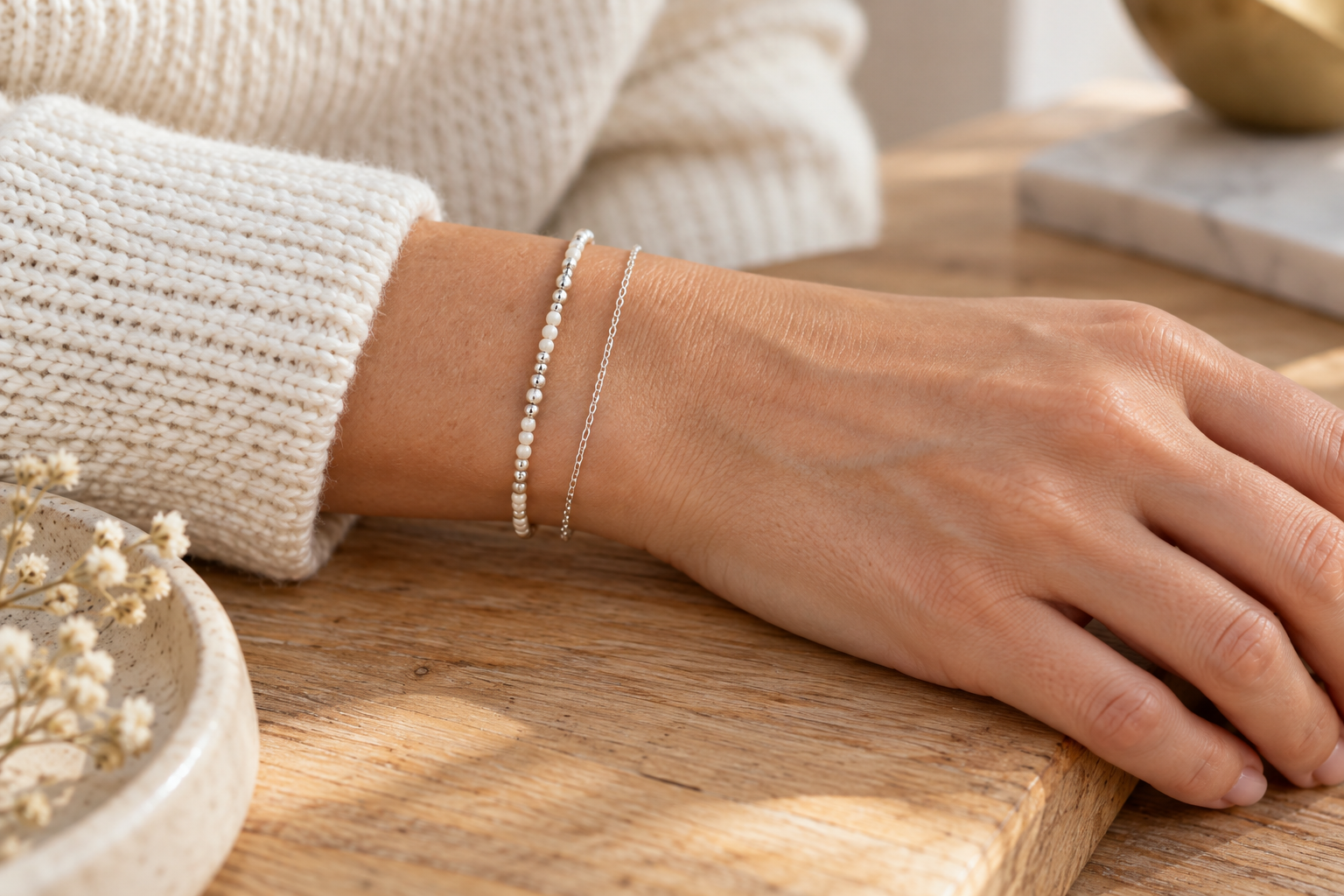 Pulsera fina de mostacillas junto a una cadena plateada sobre una manga de tejido claro