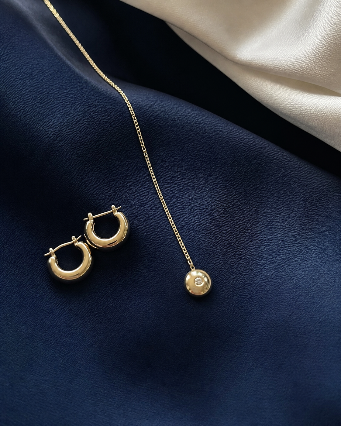 Aros dorados y collar fino sobre tela azul marino para un look de graduación