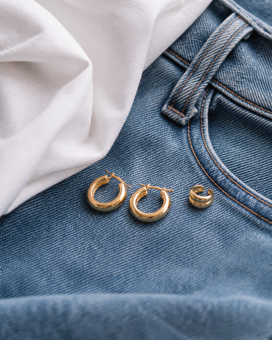 Aros dorados y ear cuff sobre jeans azules y camisa blanca