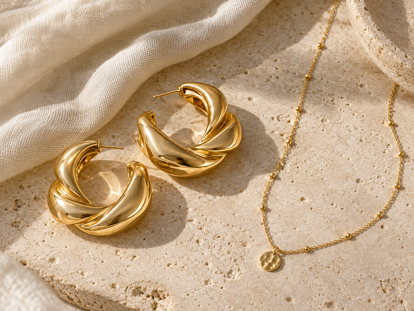 Aros escultóricos dorados y collar fino sobre lino claro, ejemplo de joyas protagonistas