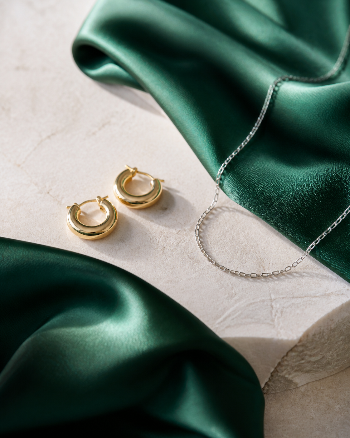Aros dorados y collar plateado sobre tela verde para comparar metales
