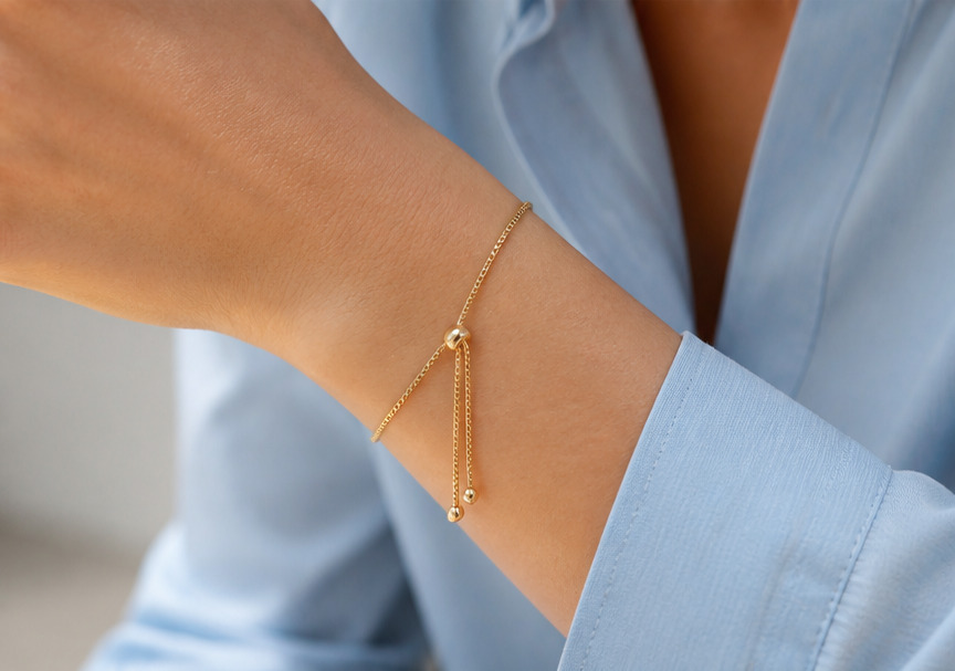 Pulsera ajustable dorada en muñeca con camisa celeste, mostrando un calce delicado