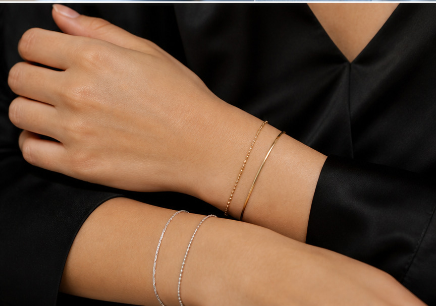 Pulseras doradas y plateadas finas combinadas sobre muñeca con blusa negra