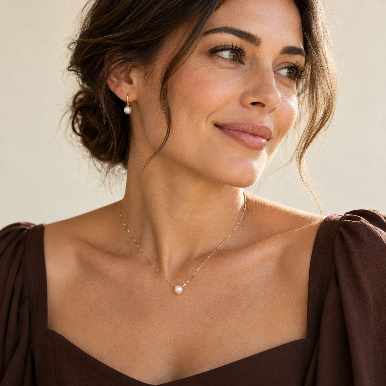 Collar delicado y aros discretos sobre el escote de un vestido café oscuro