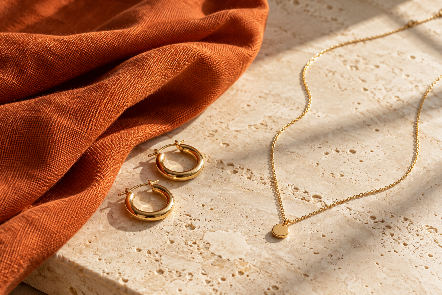 Argollas y collar dorados junto a tela naranja quemado